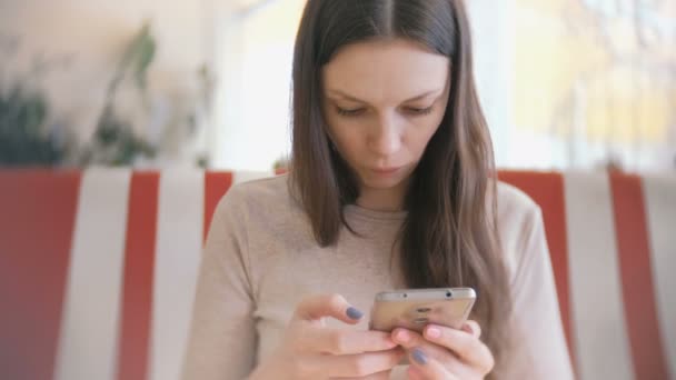 Молодая красивая женщина брюнетка просматривает интернет в своем мобильном телефоне в кафе и ждет своих друзей — стоковое видео