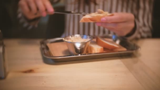 Mooie jongedame brunette uitstrijkjes tapenade op een stuk brood. Close-up dames handen met mes. — Stockvideo