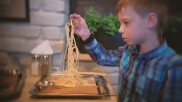 Мальчик ест спагетти в кафе и смотрит телевизор. . — стоковое видео