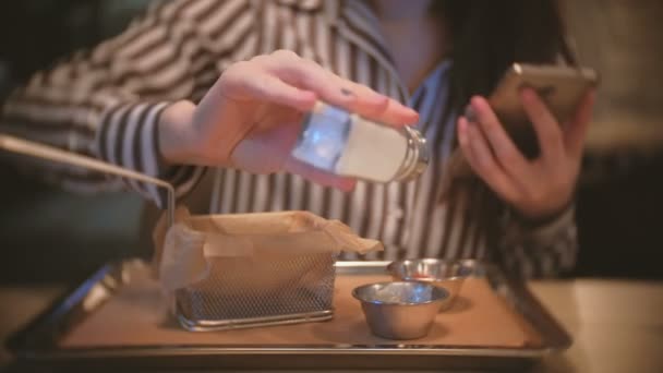 Kvinna saltning sås och äter pommes frites, doppa den i såsen. Närbild händer med mobiltelefon. — Stockvideo