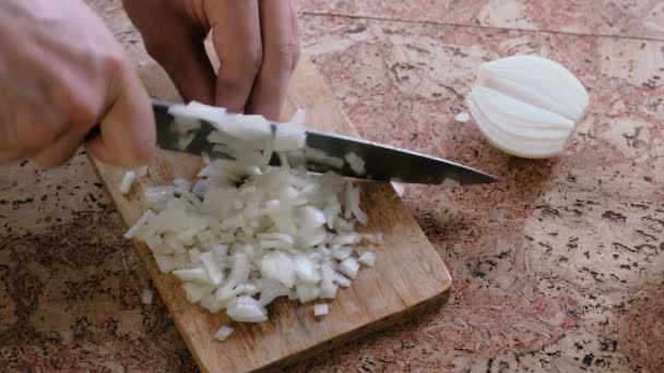 Man gently cuts the onion into small pieces and takes a wooden board with onion from the table. Close-up hands. — Stock Video