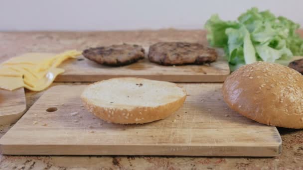 Termékeknél burgers elkészítése: zsemle, szeletek, sajt, saláta, az asztalon. Oldalnézet.