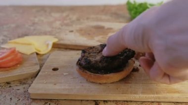 Adam burger buns, sos, domates, salatalık, beşamel sos, peynir, salata, sos, domuz pastırması ile yapar. Yakın çekim yakışıklı, yüksek hız.