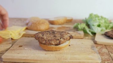 Adam burger buns, domates, salatalık, beşamel sos, peynir, salata, sos, domuz pastırması ile yapar. Yakın çekim yakışıklı.