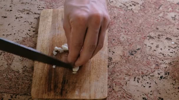 माणूस लाकडी बोर्डवर कापलेल्या कांद्यावर लसूण कापतो. बंद-अप माणसांचे हात . — स्टॉक व्हिडिओ