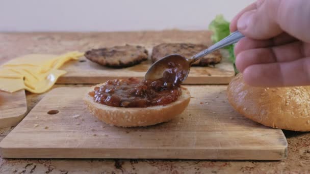 El hombre hace hamburguesa con bollos, salsa, tomates, pepinos, croquetas, queso, ensalada, salsa, tocino. Primer plano de las manos, Alta velocidad . — Vídeos de Stock