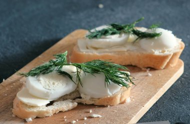 Ekmek, tereyağı, yumurta ve dereotu ahşap tahta siyah arka plan üzerinde closeup iki sandviç. Bir sandviç yapmak.