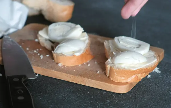 Womans tangan asin sandwich dengan roti, mentega dan telur di papan kayu di latar belakang hitam. Membuat sandwich . — Stok Foto