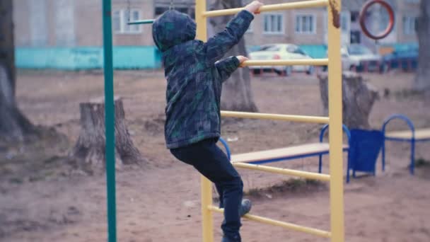 Rapaz rastejando nos bares de macacos no quintal de uma casa da cidade. Jogos e passeios no parque infantil . — Vídeo de Stock