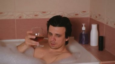 Adam bir banyo alır ve konyak içer ve ağlıyor. Depresyon ve yaşam sorunları. Yüz yakın çekim.