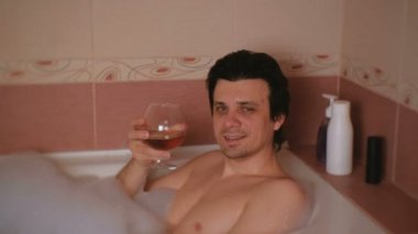 Genç adam bir banyo köpük ve içki viski gitmeyi alır. Gülümseyen ve kameraya bakıyor.