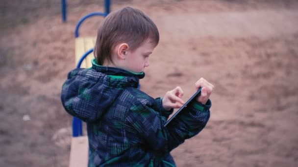 Jongen raakt een scherm van de tablet zitten in het Park op een bankje. Zijaanzicht. — Stockvideo