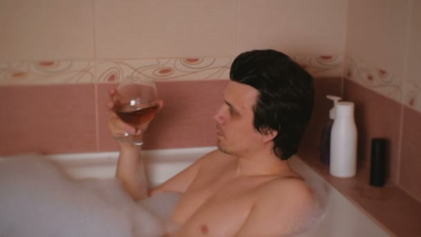 El joven se baña con espuma y bebe whisky. Descanso y relajación después del trabajo . — Vídeos de Stock