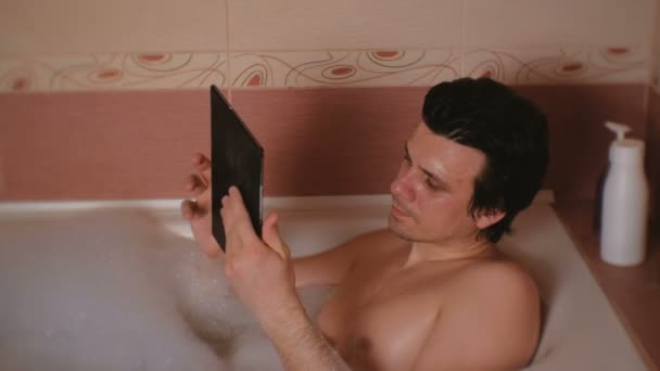 Ung mann bader, leser Internett på nettbrettet . – stockvideo
