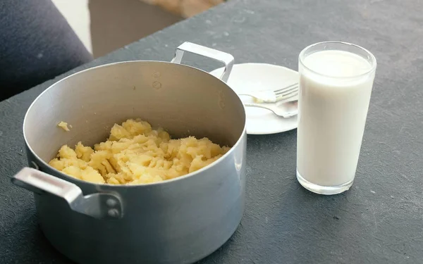 Kartoffelbrei im Topf zubereiten. Glas Milch auf dem Tisch. — Stockfoto