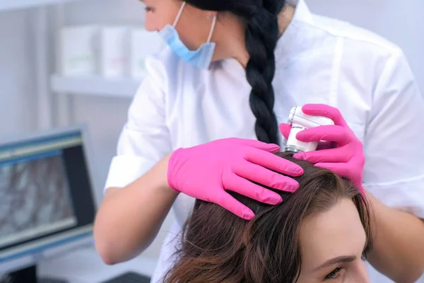 Dokter tricholoog onderzoekt vrouwelijke patiënten haren met behulp van trichoscoop in de kliniek. — Stockfoto