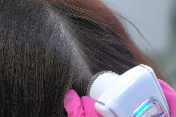 Lékař tricholog vyšetřuje ženy vlasy pomocí trikhoskopu na klinice. — Stock fotografie