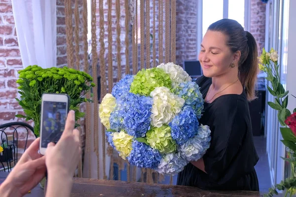 Kwiaciarnia kobieta pozowanie do zdjęć na telefon z ogromnym bukiet kwiatów hortensji. — Zdjęcie stockowe