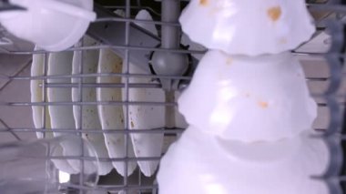 Mans el bulaşık makinesinin üst sepetine beyaz kirli bardak koyar ve mutfak ile iter.