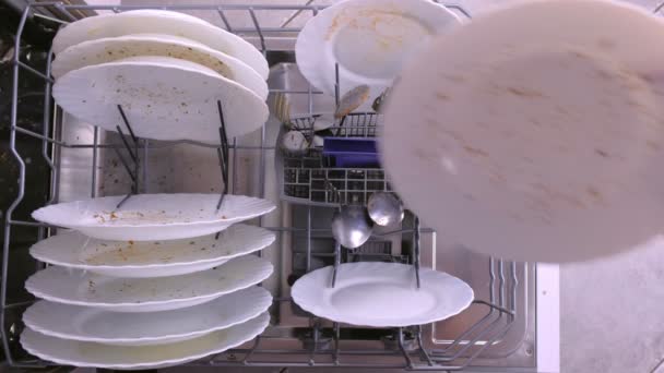 Mans hand puts white dirty plates and spoon in dishwasher basket. — Stock Video