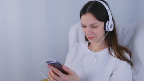 女性はスマート フォンでヘッドフォンで音楽を聴く. — ストック動画