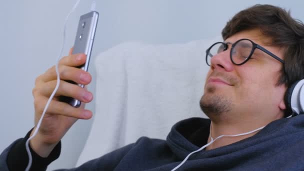 Homme écoute de la musique dans les écouteurs sur smartphone et chante une chanson dans le karaoké. Détendez-vous les yeux fermés . — Video