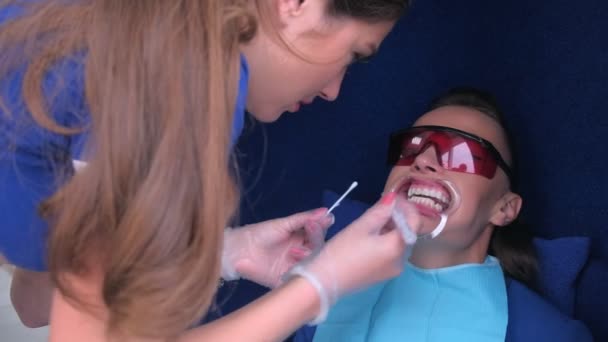 Dentist applying gel for LED whitening to woman patients teeth in dentistry. — Stock Video