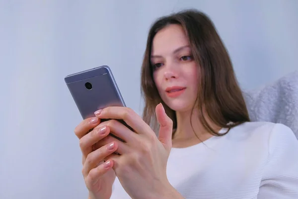 Mujer morena joven está leyendo un libro en el teléfono móvil sentado en el sillón . — Foto de Stock