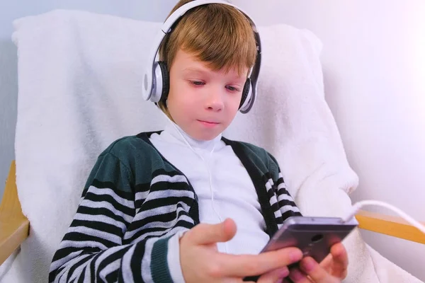 Junge sieht Video mit Kopfhörer in Handy im Sessel. — Stockfoto