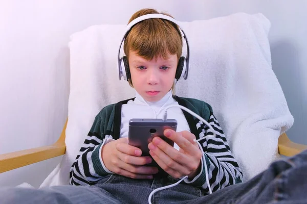 Junge sieht Video mit Kopfhörer in Handy im Sessel. — Stockfoto