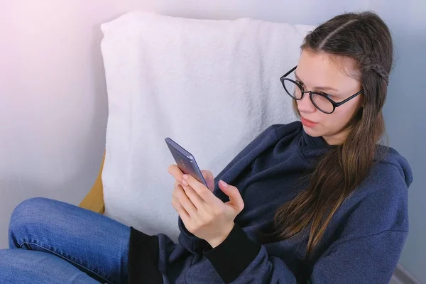 Ung brunette kvinne i briller skriver en beskjed på en mobiltelefon. Sett fra siden . – stockfoto