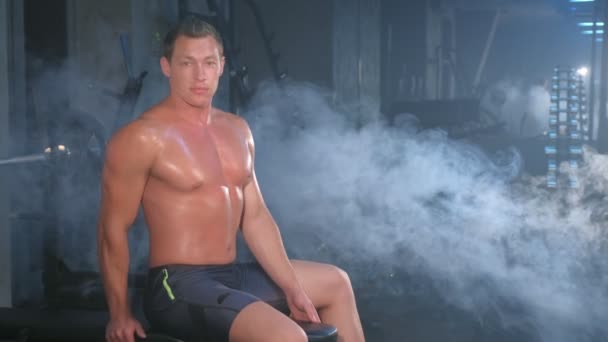 Porträtt professionell muskelatletisk man bodybuilder sitter på bänk i gym. — Stockvideo