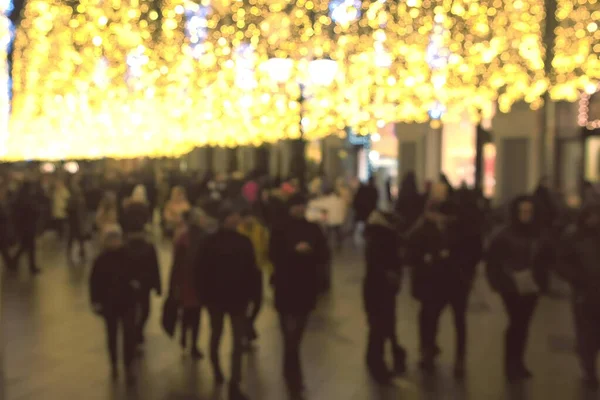 People walk on the street with golden christmas lights decorations, blur background.