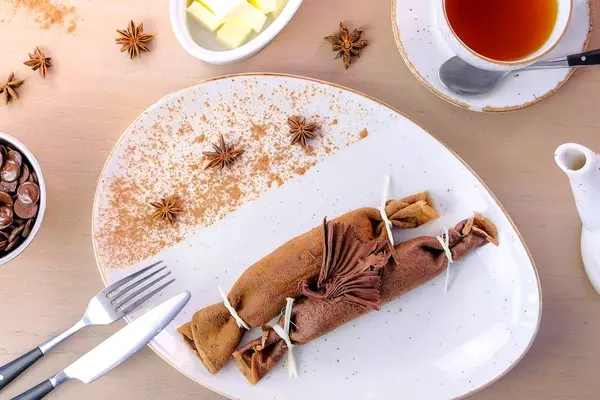 Schokolade russische Pfannkuchen, Blini mit Quarkfüllung auf dem Teller. serviert mit einer Tasse Tee und Butter. Ansicht von oben. — Stockfoto