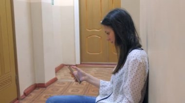 Genç kadın kapı yakınında oturan telefon tarama iş görüşmesi için sırasını bekliyor.