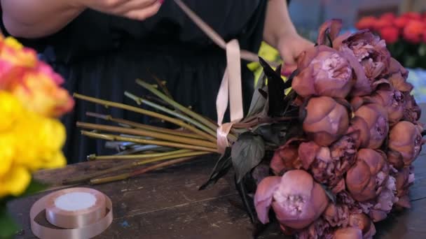 Femme fleuriste liens tiges par rubans sur bouquet de pivoines brunes dans la boutique de fleurs .