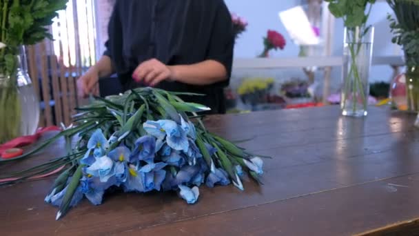 Жінка-флорист готує квіти ірису для букета в квітковому магазині на дерев'яному столі . — стокове відео