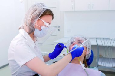 Dental hygienist makes ultrasonic teeth cleaning for young woman in dentistry.
