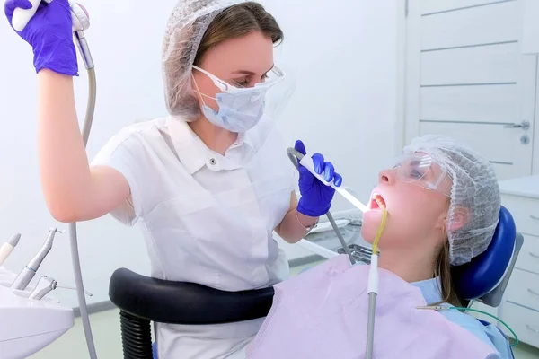 Dental hygienist makes ultrasonic cleaning pours teeth with water to woman.