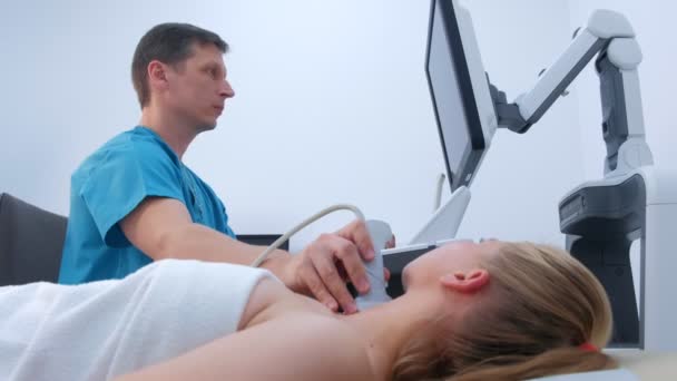 Doctor makes ultrasound scanning diagnostic of thyroid gland to woman in clinic. — ストック動画