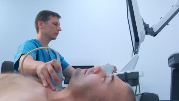 Hombre médico examinando mans paciente glándula tiroides utilizando un escáner de ultrasonido . — Vídeos de Stock