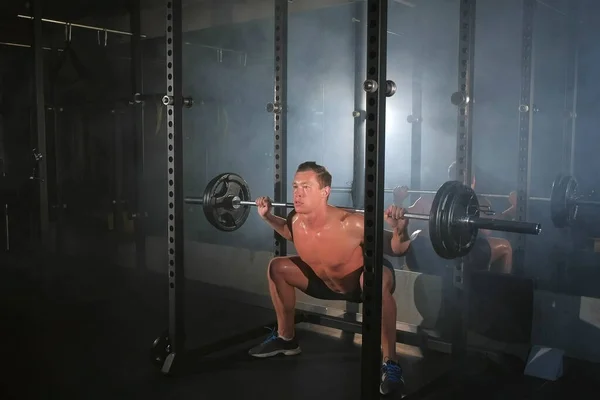 Hombre culturista haciendo ejercicio en cuclillas con barra de pesas en la máquina de herrería en el gimnasio . —  Fotos de Stock