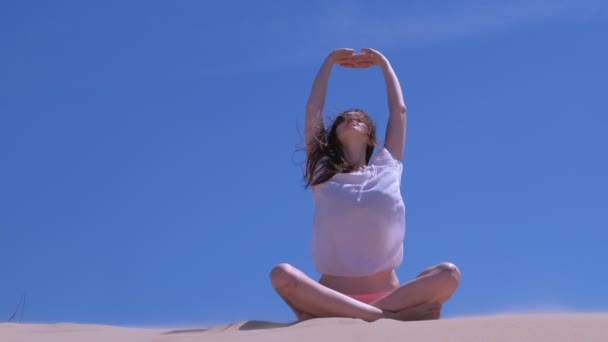 Woman stretch sits lotus pose sandy beach hands up tilts in side windy day sky. — Stock Video