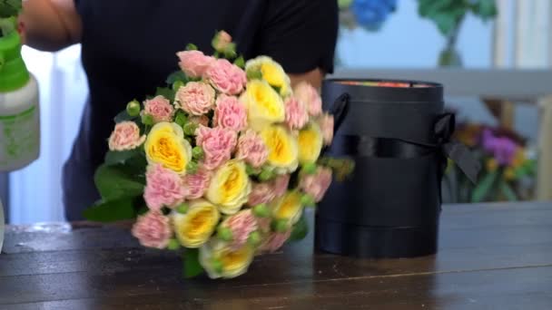 Floristería rociando flores con agua haciendo ramo de rosas poniéndolo caja . — Vídeo de stock