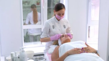 Eldivenli kozmetik uzmanı müşterileri yıkıyor. Kadın peçeteyle yüzünü siliyor..