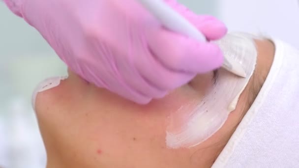 Cosmetólogo está aplicando máscara blanca en cara de cliente mujer en clínica de belleza . — Vídeo de stock