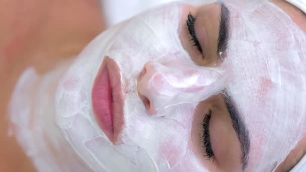 Portrait of woman laying in spa salon with white mask on face, top view. — Stockvideo