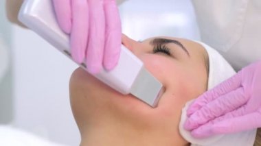 Kozmetik uzmanı klinikteki genç bayana ultrasonik yüz temizleme prosedürü uyguluyor..