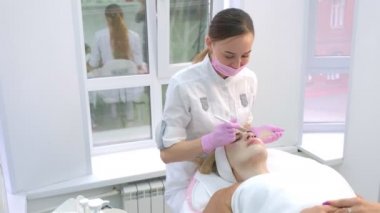 Kozmetik uzmanı klinikteki kadın hasta yüzüne cilt bakımı için maske takıyor..