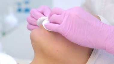 Eldivenli kozmetik uzmanı müşterileri temizliyor. Kadın yüzünü pamukla siliyor..